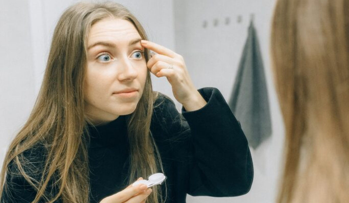 woman-looking-in-the-mirror-as-she-puts-on-contact-lenses