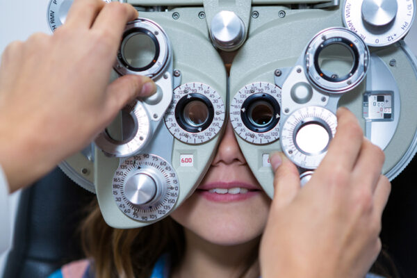 Female optometrist examining young patient on phoropter in ophthalmology clinic.