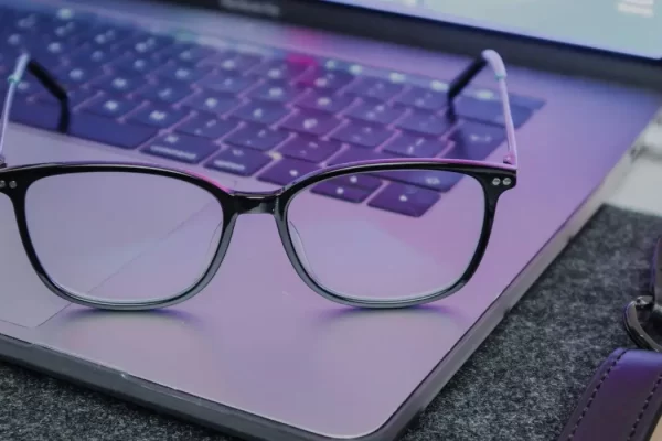 A pair of blue light blocking glasses resting on a laptop keyboard, designed to reduce dry eyes associated with prolonged screen use.