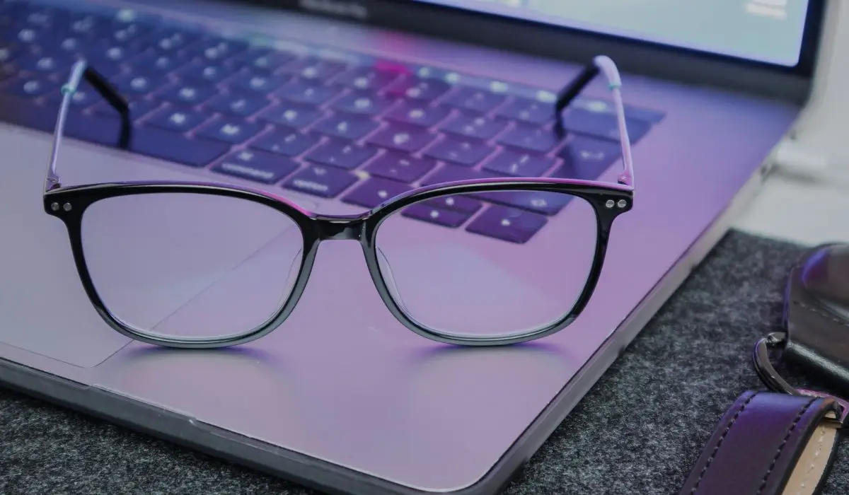 A pair of blue light blocking glasses resting on a laptop keyboard, designed to reduce dry eyes associated with prolonged screen use.