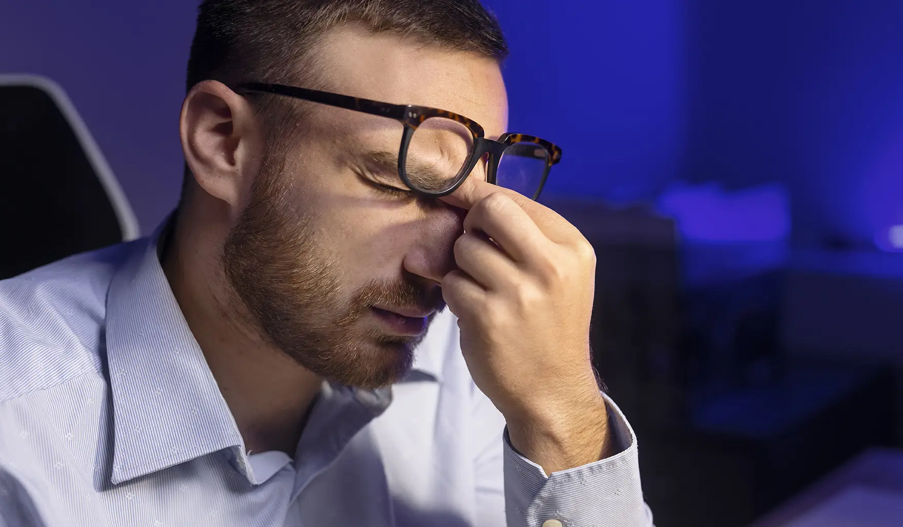 A man experiencing discomfort from digital eye strain, pressing the bridge of his nose for relief after screen time.