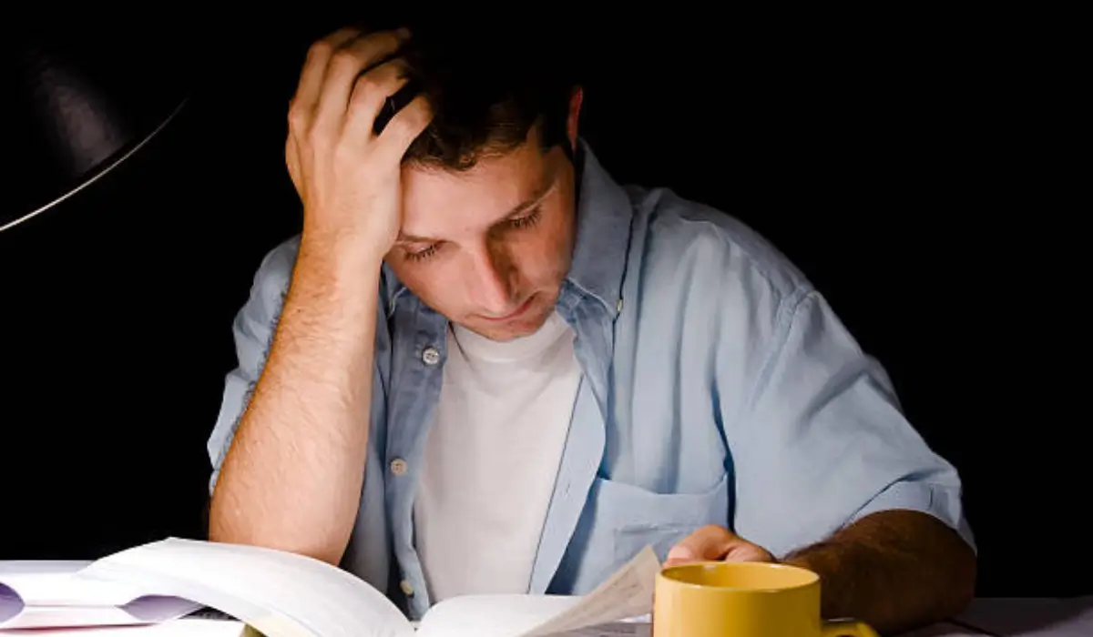 A young man reading under poor lighting, straining his eyes, highlighting the importance of vision health.