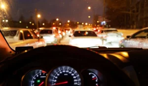 Night driving traffic view with glare and brake lights through car windshield.