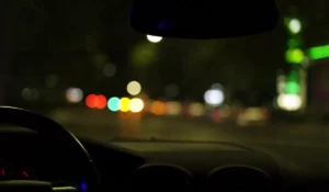 Blurry streetlights and halos seen from a car windshield, showing light sensitivity symptoms during night driving.