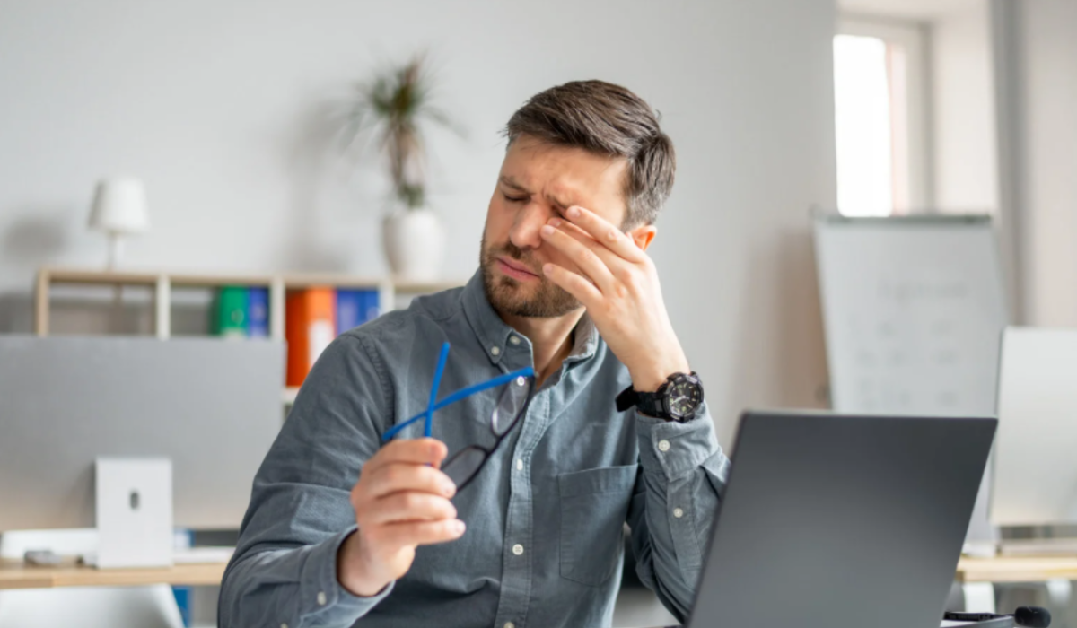 Office professional experiencing digital eye strain while working long hours on laptop screen.